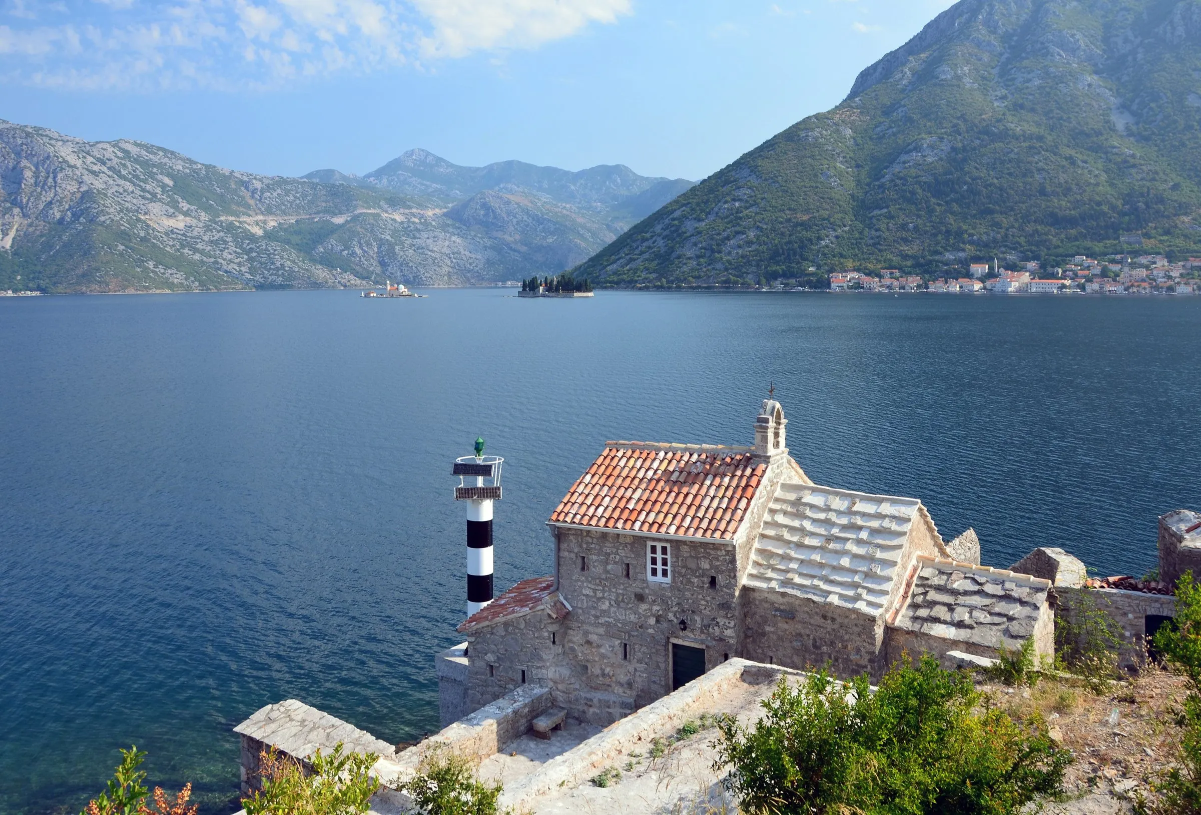Zatoka Kotorska z drogi w Lepetane: kamienna kaplica, latarnia, góry, Perast w tle